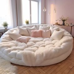 a large white round couch with pillows on it in a living room next to a window