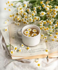 a cup of tea on top of an open book next to some daisies and flowers