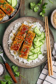 two plates with rice, cucumbers and tofu on them next to chopsticks