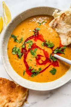 a bowl of soup with bread and garnish on the side, next to a slice of lemon