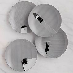 three plates with black and white designs on them, one has a cat holding an umbrella