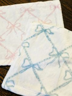 two napkins with blue and pink designs on them sitting on a wooden table next to each other