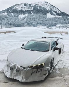 a silver sports car covered in snow on the side of a road with mountains in the background