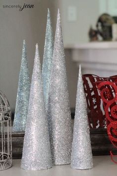 three silver christmas trees sitting on top of a white table next to a red pillow