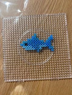 a small blue beaded animal sitting on top of a wooden table next to a plastic bag