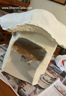 a paper mache house sitting on top of a table next to magazines and papers