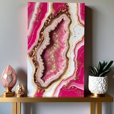 a pink and gold art piece on a shelf next to a potted succulent