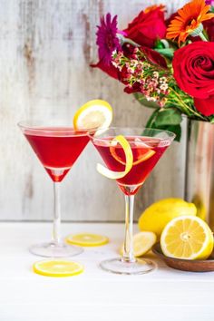 two glasses filled with red and yellow cocktails next to some cut up lemons