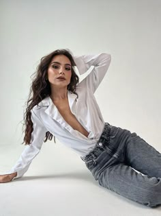 a woman sitting on the ground with her hands behind her head, wearing jeans and a white shirt