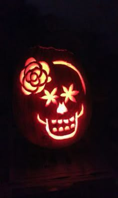 a pumpkin carved to look like a skull with roses on it's face, lit up in the dark