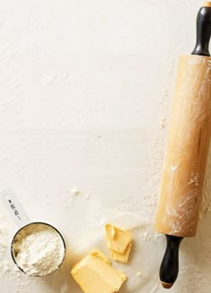 a rolling pin and some cheese on a table next to a measuring cup filled with flour