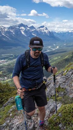 a man hiking up the side of a mountain in shorts and a hat with ski poles