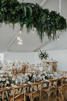 tables and chairs are set up in a tent with greenery hanging from the ceiling