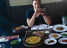 a man sitting at a table with many plates of food and chopsticks in front of him