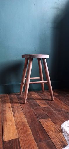 a wooden stool sitting on top of a hard wood floor next to a blue wall