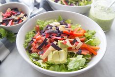 two white bowls filled with lettuce, carrots and avocado salad