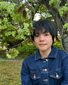 a young boy sitting under a tree with his hands on his hips and looking at the camera