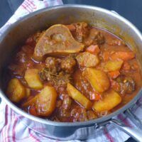 a pot filled with stew and meat on top of a table next to a napkin