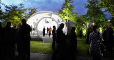 a group of people standing in front of a white tent at night with lights on