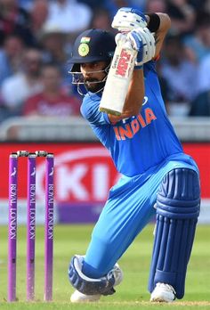 a man in blue uniform playing a game of cricket on grass with people watching from the stands