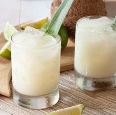 two glasses filled with white liquid next to limes and a slice of pineapple