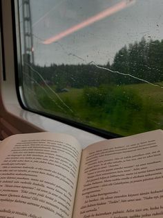 an open book sitting on top of a window sill next to a grass covered field