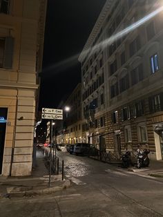 an empty city street at night with cars parked on the side and buildings in the background