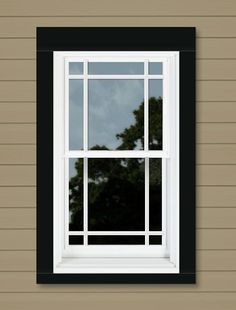 a window on the side of a red building with trees in the distance behind it