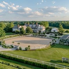 an aerial view of a horse farm with a white fenced in area surrounded by green grass and trees