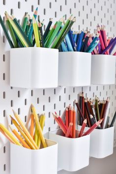 pencils and markers are lined up in white cups on a wall mounted organizer rack