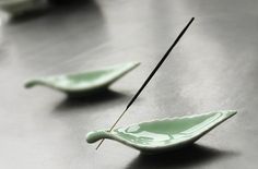 two small green bowls with sticks sticking out of them on a metal surface, one is empty and the other has a black stick in it's mouth