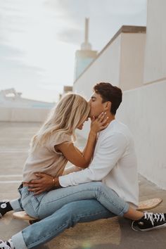 a man and woman sitting on top of a skateboard kissing in front of a building