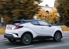 the rear end of a white toyota c - hr driving on a road with trees in the background