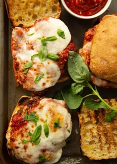 several different types of food sitting on a baking sheet next to bread and tomato sauce