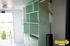 an empty room with a green bookcase and white cupboards on the wall, in front of a sliding glass door