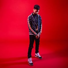 a man standing in front of a red background wearing a black and white sweater with stars on it