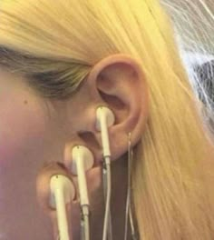 a woman with long blonde hair is wearing ear piercings and holding two white wires