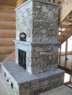 a stone fireplace sitting in the middle of a room next to a stair case and railing