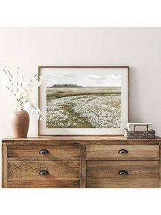 a vase with flowers sitting on top of a wooden dresser next to a framed photograph