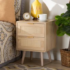 a nightstand with two drawers and a cup on it, next to a potted plant