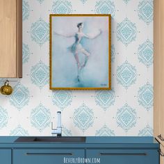 a painting hanging on the wall above a sink in a blue and white kitchen with wooden cabinets