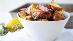 a white bowl filled with potatoes on top of a table next to lemon wedges