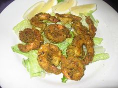 a white plate topped with lettuce and shrimp next to lemon wedged slices