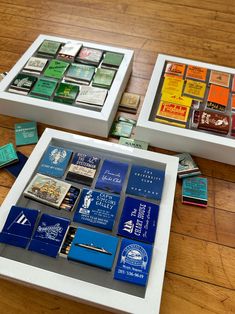 two white boxes filled with different types of matchboxes on top of a wooden floor