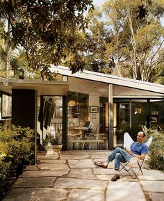 a man sitting in a lawn chair on top of a stone patio next to a house