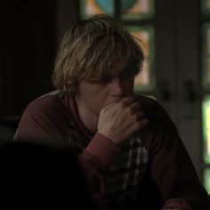 a man sitting at a table with his hands clasped to his face in front of stained glass windows