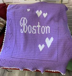 a crocheted blanket with the word boston written in white on it and hearts