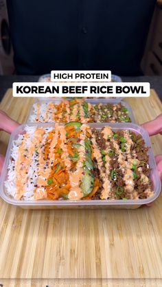 a person holding up a tray of korean beef rice bowl on top of a wooden table