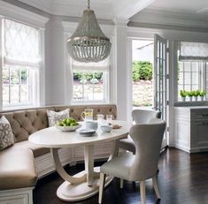 a white dining room table with chairs around it and a bench in the corner between two windows