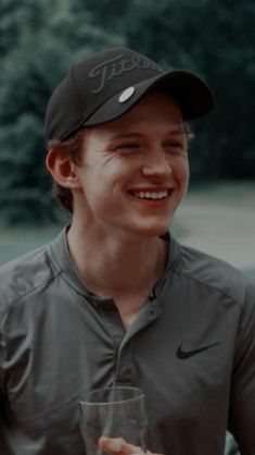 a young man holding a glass in his hand and smiling at the camera while wearing a nike hat